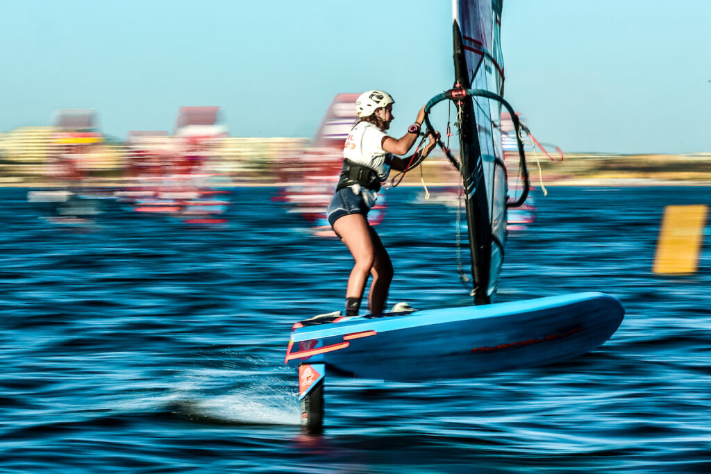 Emma Schleicher foilt auf ihrem Surfboard. Der Hintergrund ist verschwommen.