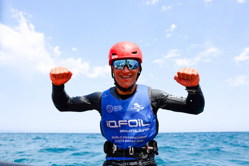 Ein Mann mit einem blauen Trikot, verspiegelter Sonnenbrille und einem roten Helm jubelt auf dem Wasser.