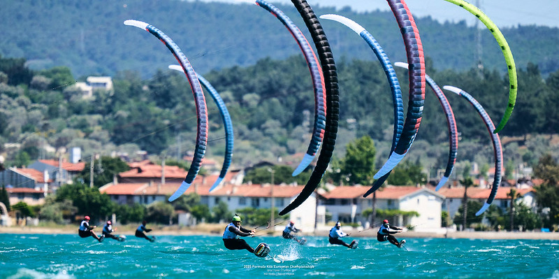 Sieben Kitesurfer fahren über das Wasser des Mittelmeeres auf den Betrachter zu.