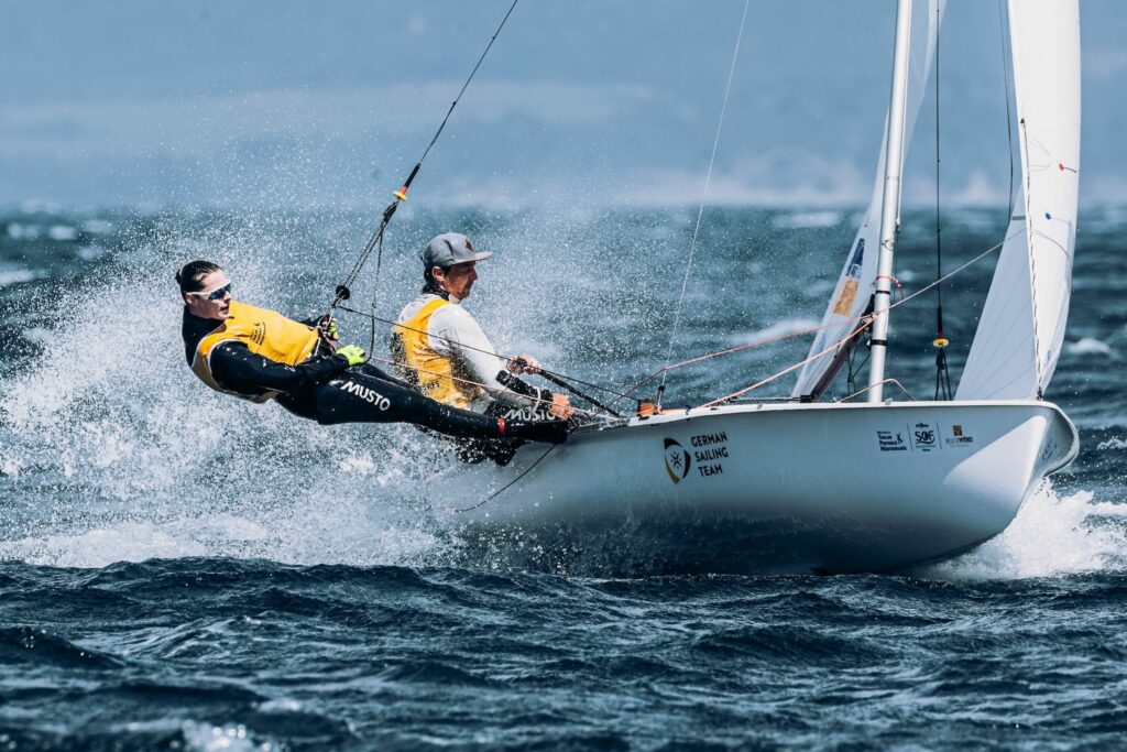 Simon Diesch und Anna Markfort segeln bei starkem Wind ihre 470er-Jolle. Simon Diesch steuert, Anna Markfort steht im Trapez. Beide tragen ein gelbes Leibchen. 