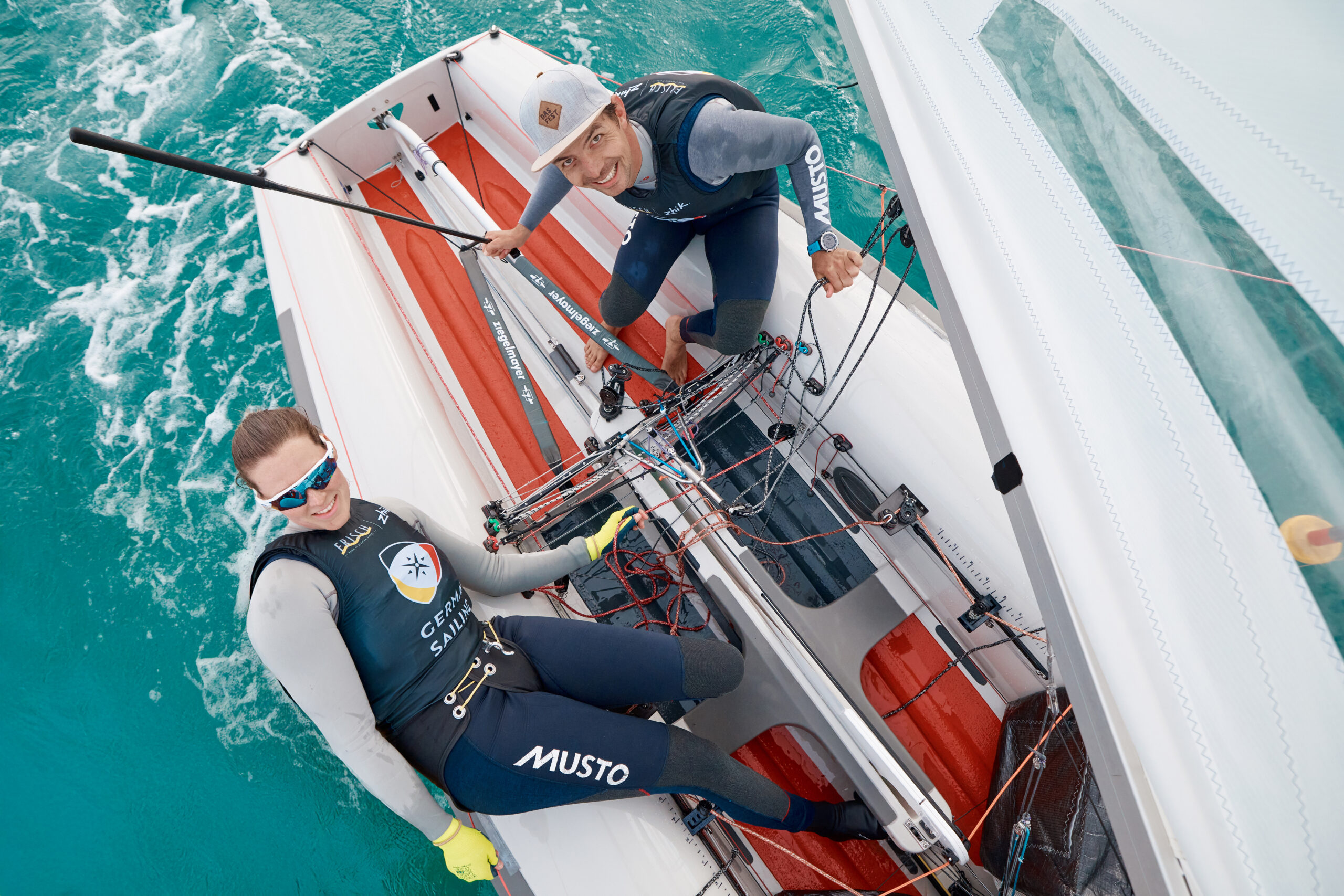 Simon Diesch und Anna Markfort sitzen auf ihrem 470er und lächeln nach oben in die Kamera