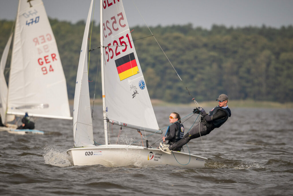 ine Seglerin und ein Segler auf einer 420er Jolle, Auf dem Rumpf steht German Sailing Team, im Segel ist die Nummer 55251, eine Deutschlandflagge und die Logos von zwei Sponsoren.