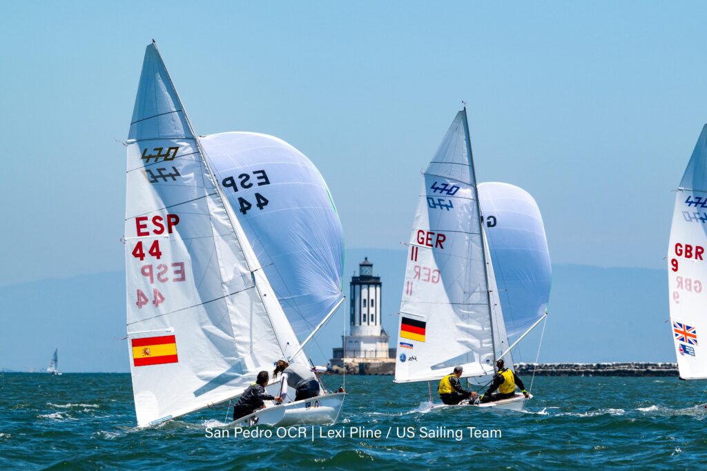 470er segeln unter Spinnaker, im Hintergrund ist ein Leuchtturm zu sehen