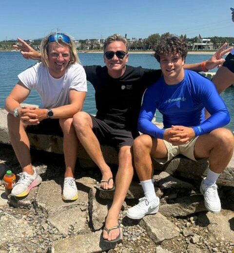 Jannis Maus, DSV-Trainer Aleksei Chibizov und Jan Vöster sitzen auf einer Mauer. Sie lächeln in die Kamera. Im Hintergrund ist das Meer zu sehen