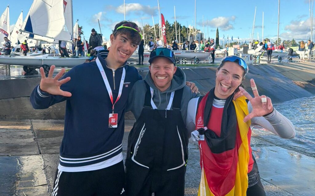 Levian Büscher, Choach Fabian Kirchhoff und Mirja Dohle lachen in die Kamera. Mirja hat eine Deutschland-Flagge umhängen.